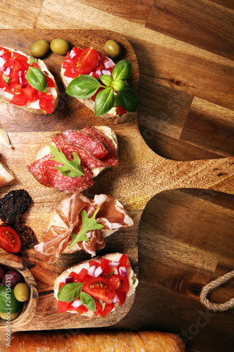 antipasto various appetizer. Cutting board with prosciutto, salami, cheese, bread and olives on dark wooden background