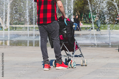 Lonely single father hipster in checkered red and black shirt with a stroller walking in the city park