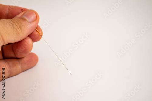 Hand of an acupuncturist holding a long thin acupuncture needle. Man's hand and metal needle.