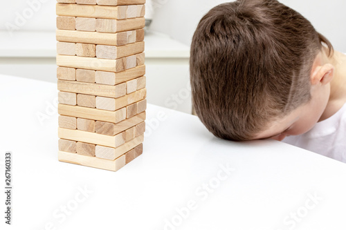 A bored preteen caucasian boy trying to play wooden block tower board game to entertain himself