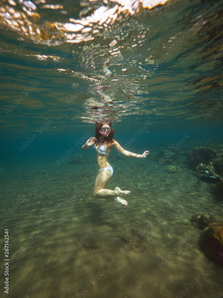Young woman with snorkel mask and tube swimming underwater in sea on coral reef background. Girl with snorkeling mask and snorkel under sea water. Apo Island, Philippines.