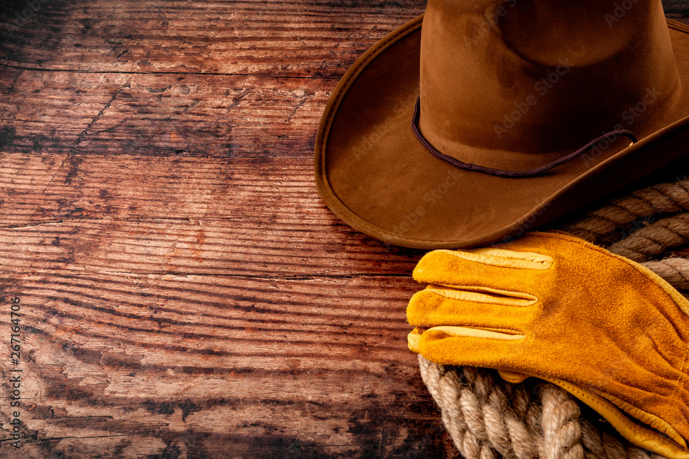 American culture, living on a ranch or farm and country muisc concept theme with a cowboy hat, rope lasso and rodeo leather gloves on a wooden background in a old saloon with copy space - obrazy, fototapety, plakaty 