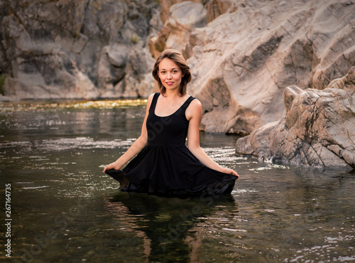 Young woman with a black dress standing in a creek  looking at the camera