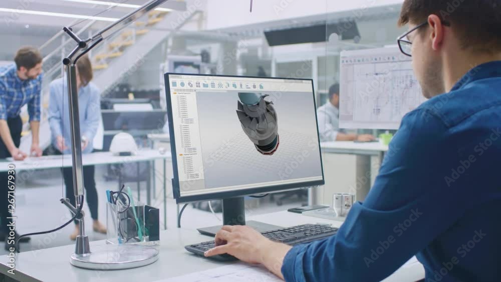 Engineer Working on Desktop Computer, Screen Showing CAD Software with 3D Engine Prototype. In the Background Engineering Facility with Blueprints and Drawings. Over the Shoulder