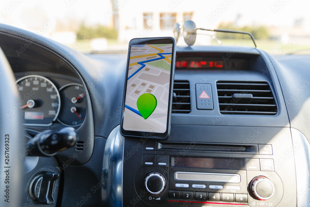 The map on the phone in the background of the dashboard. Black mobile phone with map gps navigation fixed in the mounting. App map for travel. The map on the phone in the background of the dashboard. Black mobile phone with map gps navigation fixed in the mounting. App map for travel.