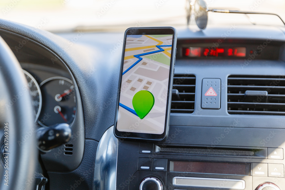 The map on the phone in the background of the dashboard. Black mobile phone with map gps navigation fixed in the mounting. App map for travel.