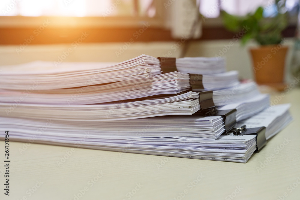 Education concept: Close and selective focus of unfinished homework assignment stack archives with binder paper clips on teacher’s desk in university waiting to be evaluated and scored. Stack of white
