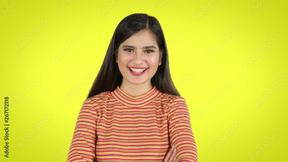 Cheerful young woman looking at the camera and laughing in the studio. Shot in 4k resolution with yellow background
