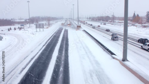Team of huge snowplows clear highway/freeway in a blizzard. During a blizzard, snowplows are clearing the snow followed by a traffic jam pileup of cars. 
