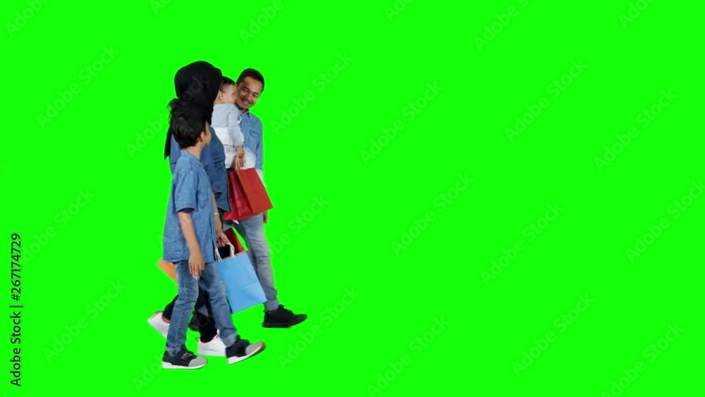 Side view of happy muslim family carrying shopping bags while walking in the studio. Shot in 4k resolution with green screen background