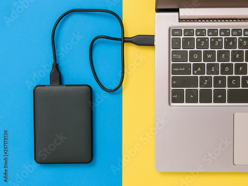 Black hard drive and laptop on yellow and blue background. Flat lay. The concept of backup storage.