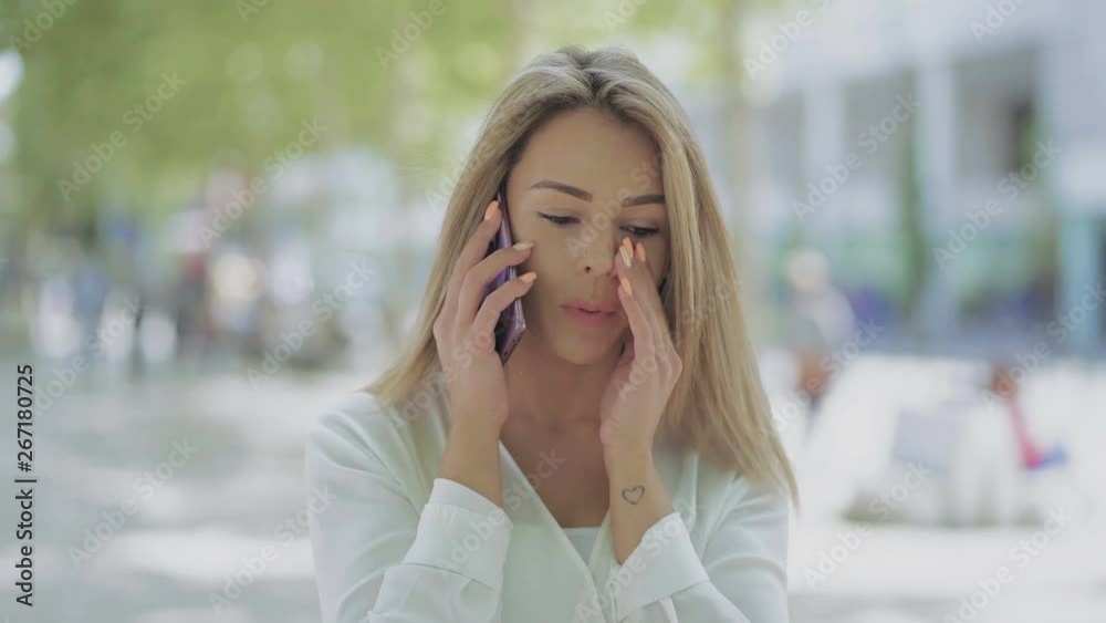 Upset young woman talking by smartphone outdoor. Stressed young woman having on street and having unpleasant phone conversation. Connection concept Upset young woman talking by smartphone outdoor. Stressed young woman having on street and having unpleasant phone conversation. Connection concept