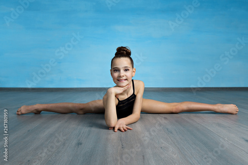 A portpait girl gymnast in a black gymnastic swimsuit is sitting on a cross splits on the blue sky background. photo