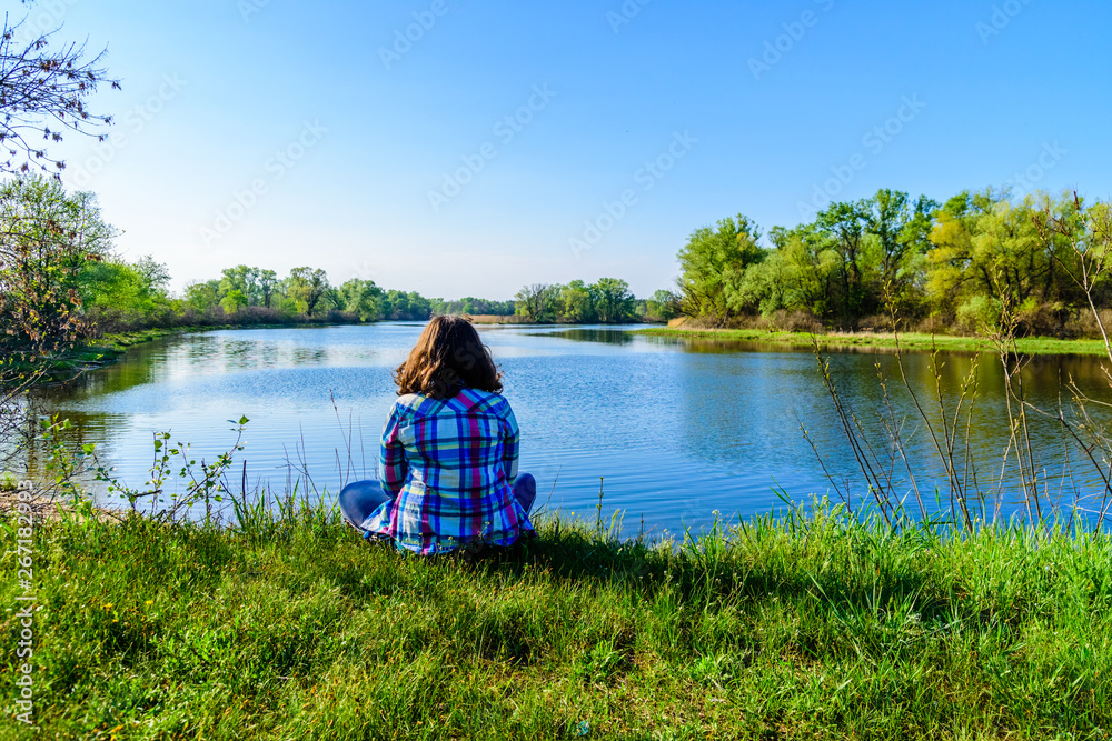 Obraz premium Lonely young woman sitting on a bank of the river