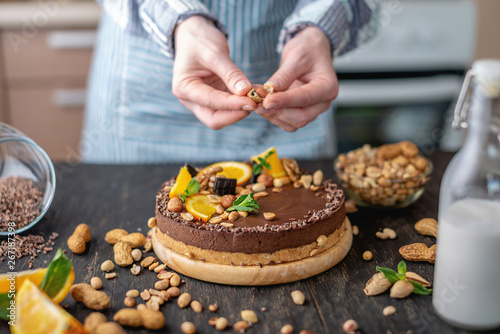 Confectioner decorates chocolate cake with orange and mint leaves with nuts. Concept healthy raw desserts for vegan food