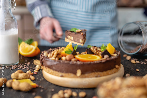 Pastry chef in hand holding a piece of chocolate cake with orange, mint and nuts. Healthy raw desserts for vegan food © Artem