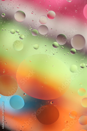 Oil drops in water on a colored background. Bright background with pink, orange, green and blue circles of different sizes. Blur, vertical, place for text, multicolor. Concept of design.