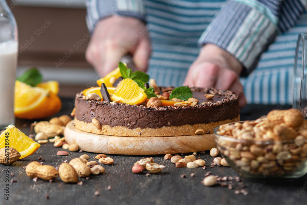 Confectioner decorates chocolate cake with orange and mint leaves with nuts. Concept healthy raw desserts for vegan food