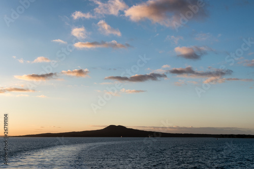 Silhouette of Rangitoto Island, Auckland, New Zealand over the ocean, with a dramatic Sunet/Sunrise and a boat wake traversing the image