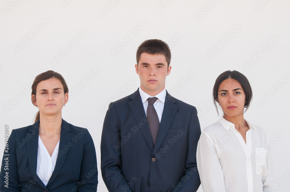 Corporate portrait of serious successful business team. Three young business people standing for camera against white background. Business team concept Corporate portrait of serious successful business team. Three young business people standing for camera against white background. Business team concept