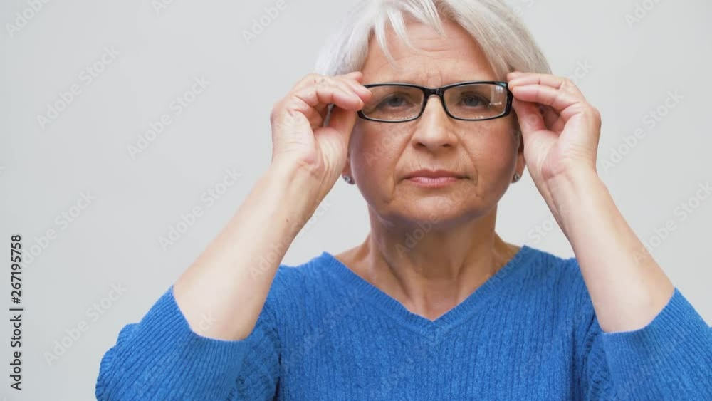 vision and old people concept - portrait of smiling senior woman putting her glasses on over grey background vision and old people concept - portrait of smiling senior woman putting her glasses on over grey background