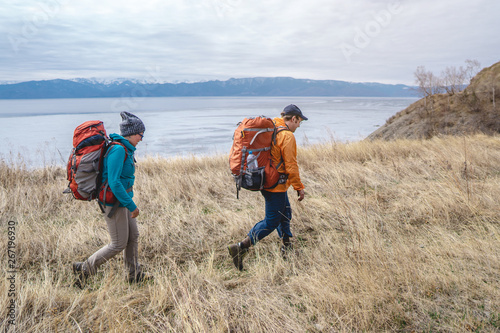 Hikers with orange backpacks go to the mountain lake. Northern Nordic nature. Concept of travel and active tourism