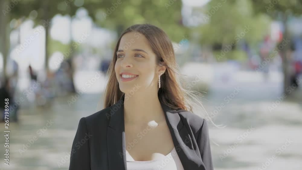 Beautiful smiling girl walking outdoor. Attractive happy young woman in suit jacket walking on street at sunny day. Emotion concept