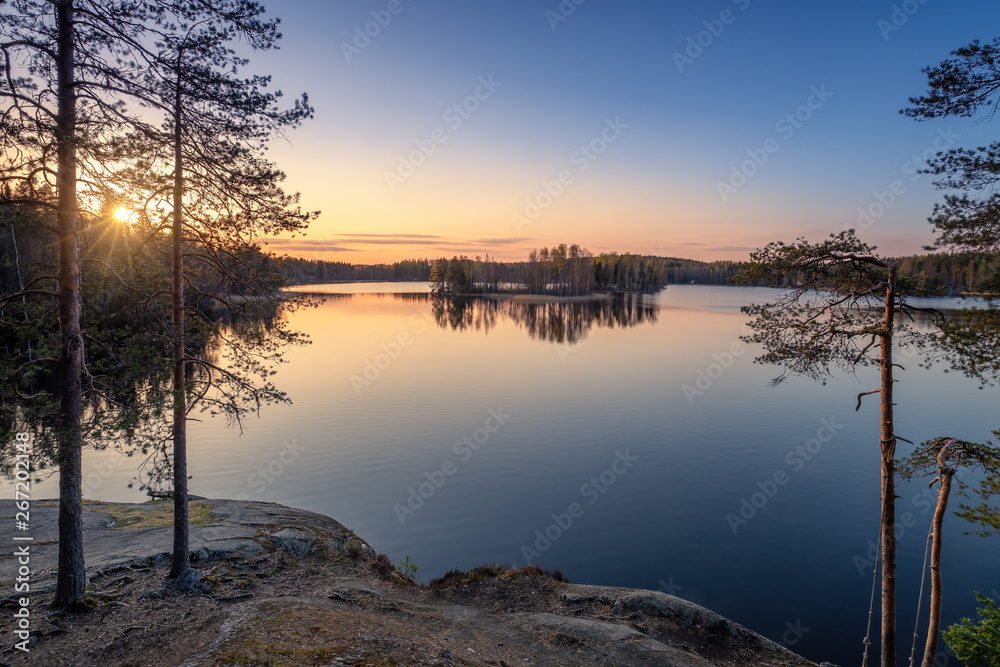 Scenic landscape with sunset, peaceful lake and tree roots at calm spring evening in Finland Scenic landscape with sunset, peaceful lake and tree roots at calm spring evening in Finland