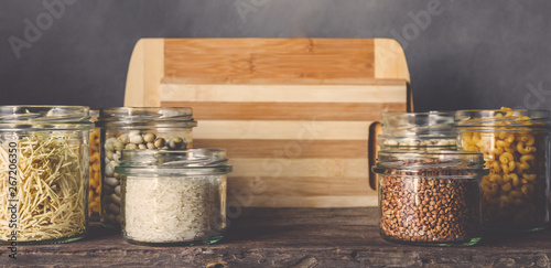 Various raw cereals, grains, beans and pasta for cooking healthy food in glass jars on a wooden table, on a gray background, Clean food, vegan, balanced diet,zero waste,eco friendly,plastic free