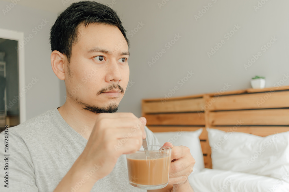 Man is drinking a cup of coffee on the bed in his bedroom. Man is drinking a cup of coffee on the bed in his bedroom.