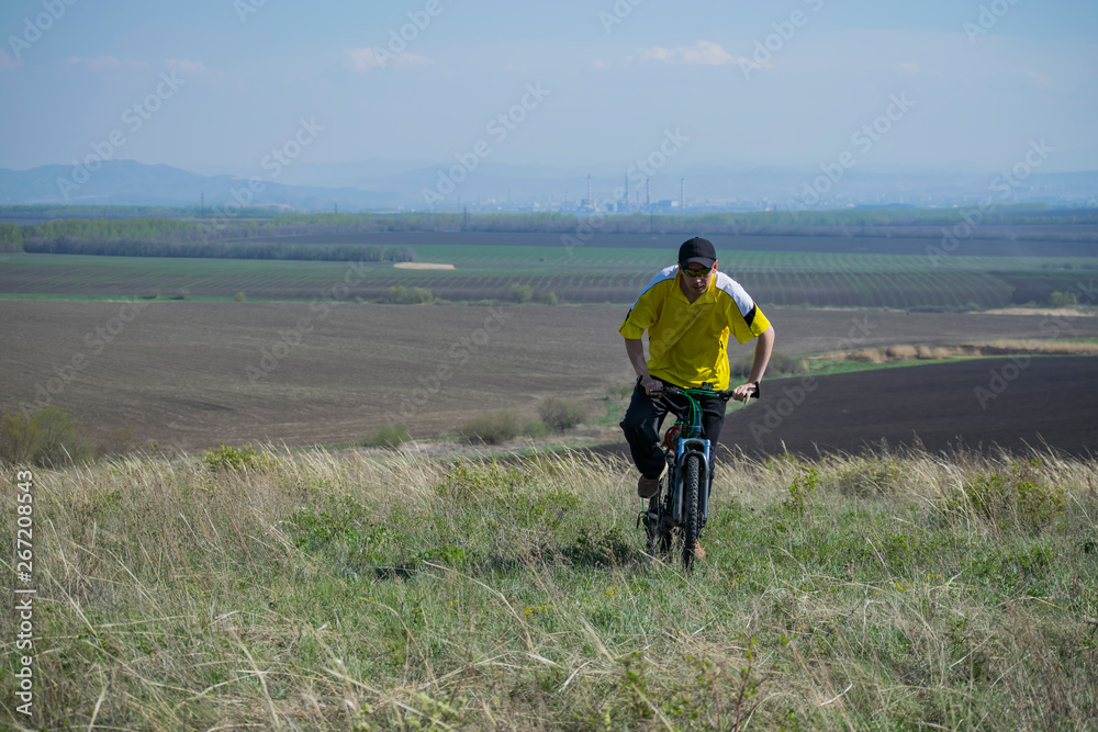 A man rides a bicycle out of town on rough terrain.