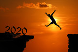 The Silhouette concept of new year 2020, Man jumping and climbing in the cave or high cliffs at a red sky sunset