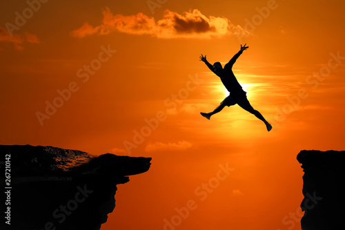 Silhouette of Men are jumped between high cliff at a red sky sunset