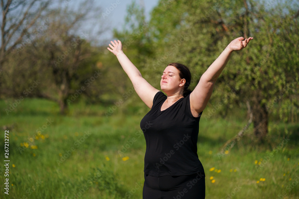 Body positive, freedom, high self esteem, confidence, happiness, obesity. Overweight woman rising hands towards the sky contemplating outdoors.