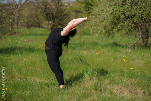Body positive, yoga, confidence, high self esteem, meditating. Young calm overweight woman doing yoga at summer meadow. obesity, wellness, outdoor activity and health.