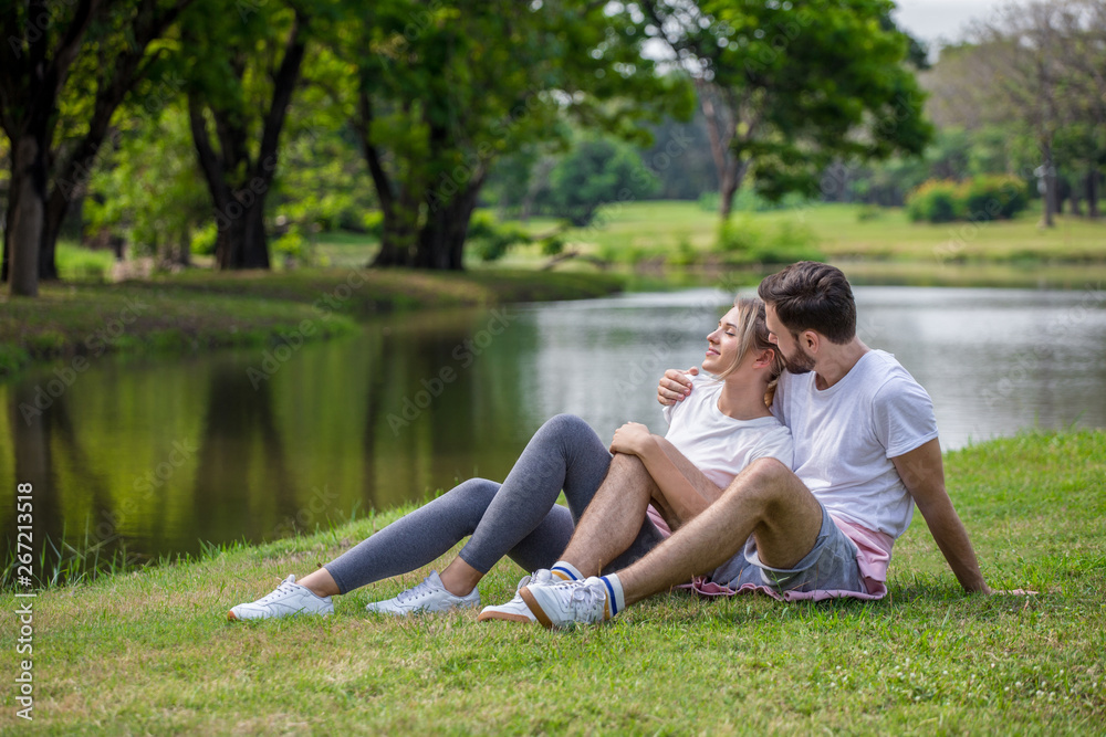 Fototapeta premium Happy young couple loving fitness in sportswear relaxing at park together in morning time. sport people sitting taking a break after exercises. resting . relationships. training,workout