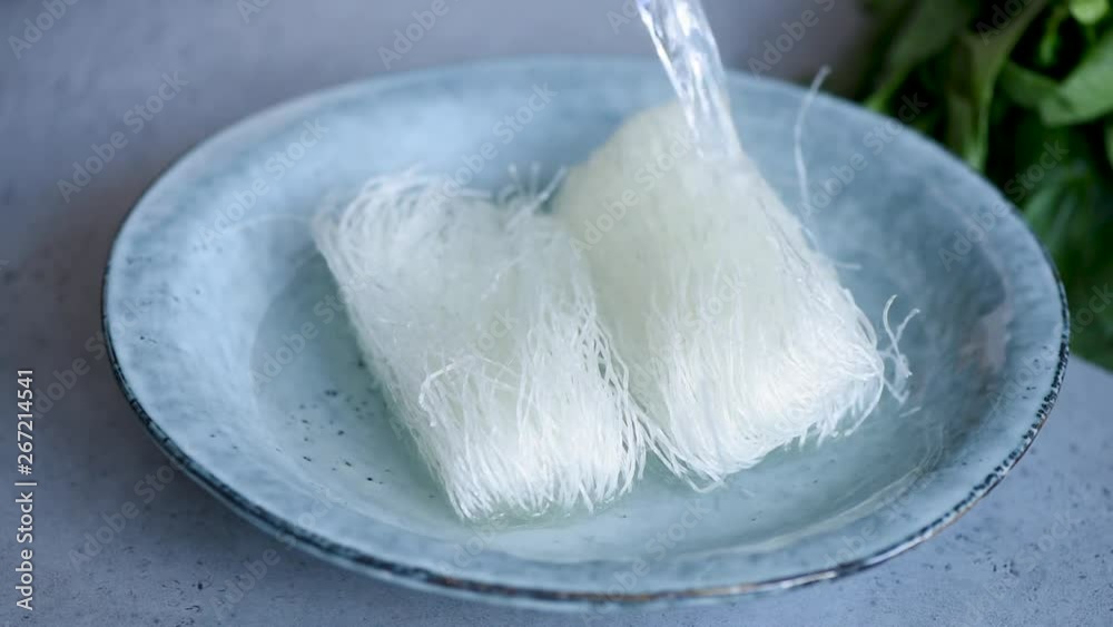 Rice glass noodles preparation. Pouring hot water in bowl with dry asian rice vermicelli or noodles