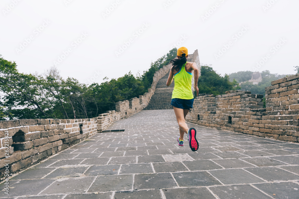 young woman trail runner running at great wall on the top of mountain