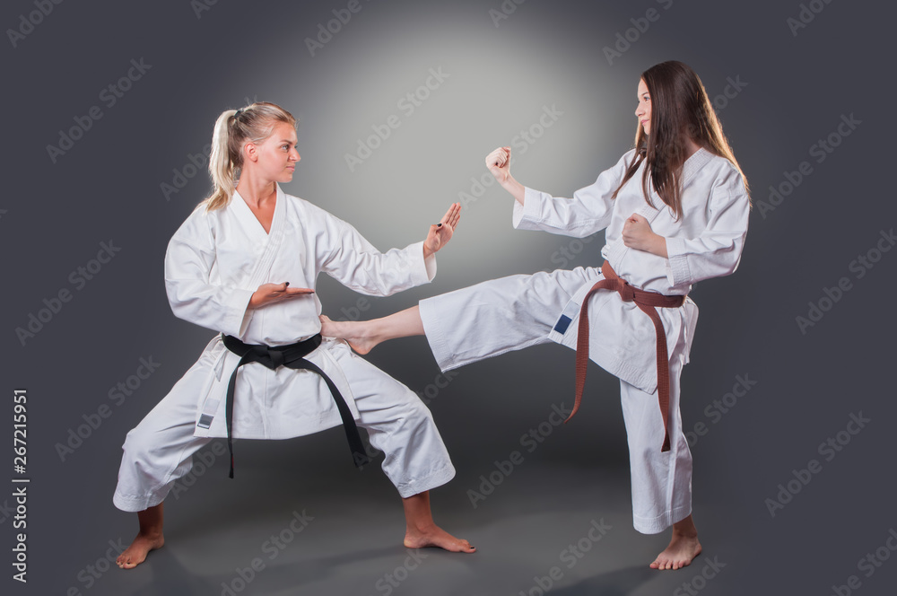 Beautiful young female karate player doing kick on the gray background Beautiful young female karate player doing kick on the gray background