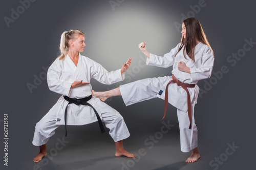 Beautiful young female karate player doing kick on the gray background