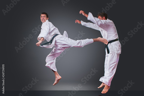 Handsome young male karate player doing kick on the gray background