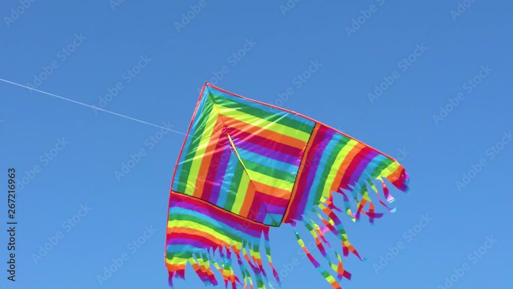 Aquilone con colori dell'arcobaleno che vola in aria con sfondo blu del cielo.