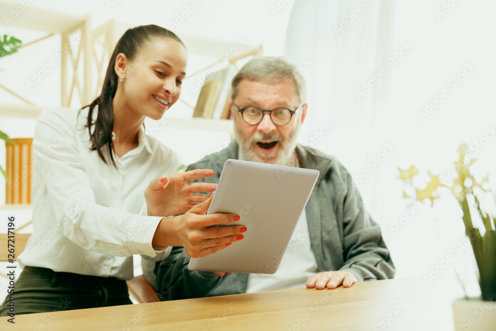 A daughter or granddaughter spends time with the grandfather or senior man. Family or fathers' day, emotions and happieness. Lifestyle portrait at home. Girl taking care about dad. Using a tablet. A daughter or granddaughter spends time with the grandfather or senior man. Family or fathers' day, emotions and happieness. Lifestyle portrait at home. Girl taking care about dad. Using a tablet.