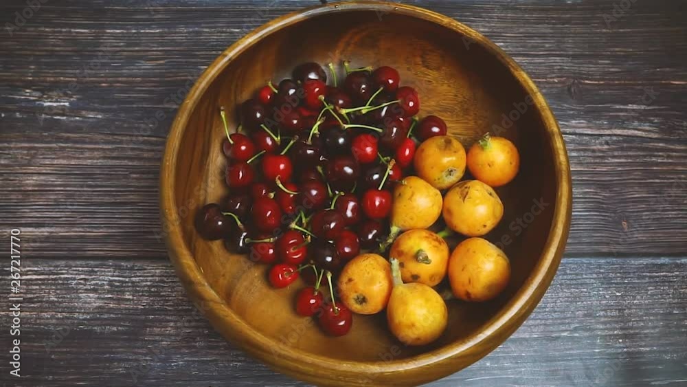 Japanese plum or Japanese medlar and cherries in wooden bowl rotating. Fresh fruits. Vegetarian healthy food concept. Japanese plum or Japanese medlar and cherries in wooden bowl rotating. Fresh fruits. Vegetarian healthy food concept.
