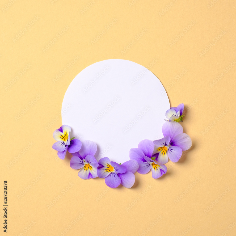 Creative flat lay composition: circle blank paper and blooming flower petals on yellow background. Top view, floral round frame, abstract design. Invitation, greeting card or element for your design