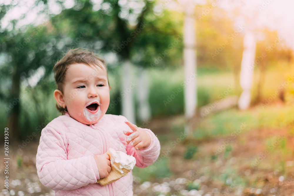 little girl in the garden on the background of greenery and trees very cute eating ice cream finger in a waffle Cup little girl in the garden on the background of greenery and trees very cute eating ice cream finger in a waffle Cup