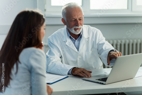 Senior doctor using laptop with female patient clinic.