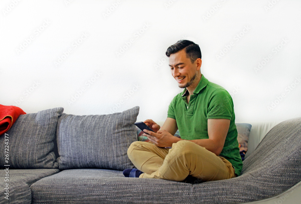 Smiling man handling smartphone while sitting on the couch Smiling man handling smartphone while sitting on the couch