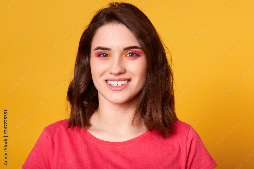 Close up portrait of beautiful caucasian young woman with pink and orange glamour make up and toothy smile, model has happy facial expression, dressed casually, posing isolated on yellow background. Close up portrait of beautiful caucasian young woman with pink and orange glamour make up and toothy smile, model has happy facial expression, dressed casually, posing isolated on yellow background.