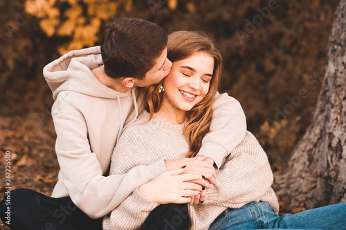 Happy love couple og teenagers sitting under tree outdoors. Boy kissing girl. Teenagerhood. photo